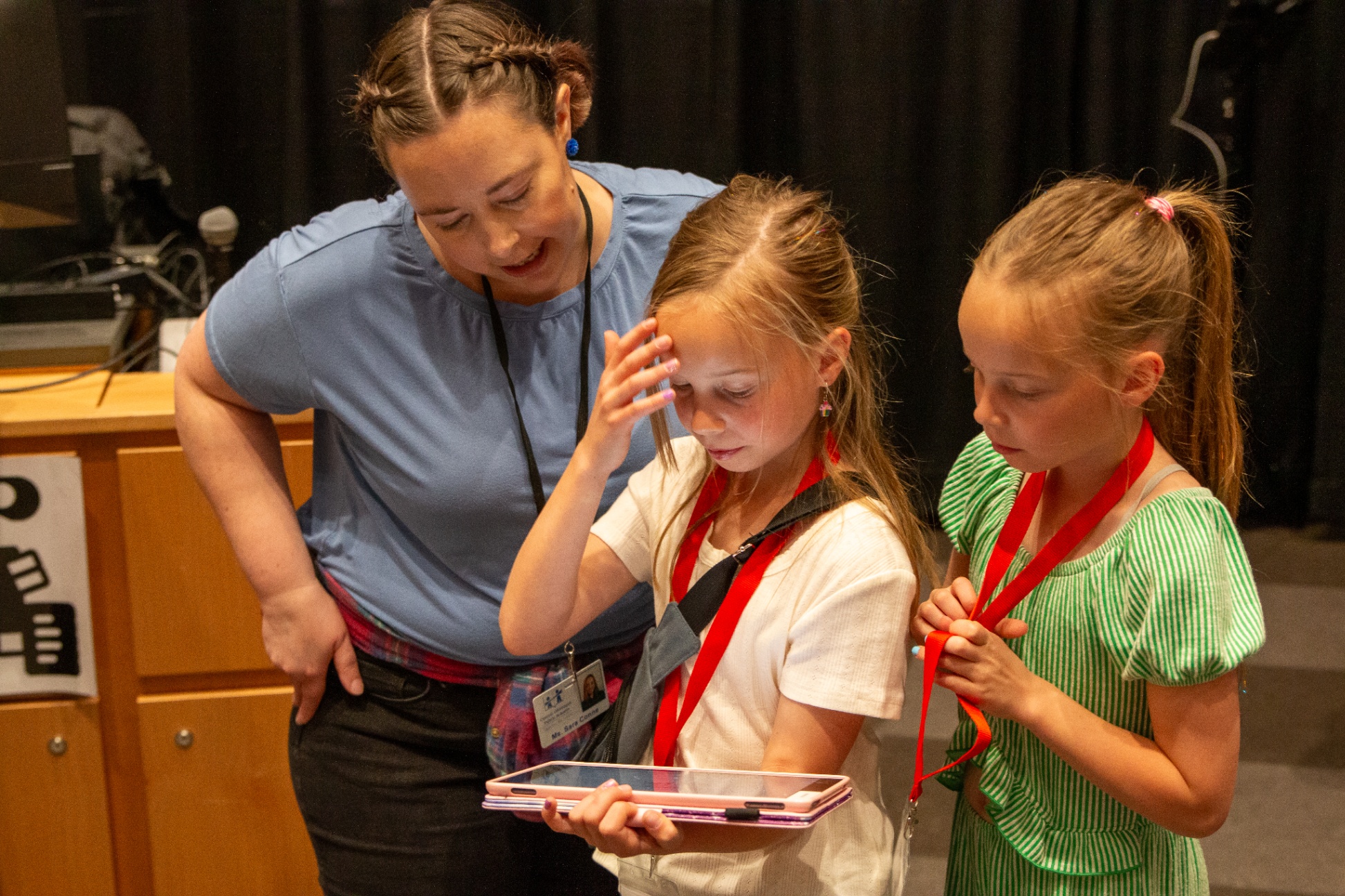 An adult helps students as they check their robot code on a tablet